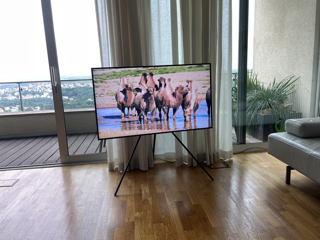 Televize na mobilním stojanu u prosklené stěny s výhledem