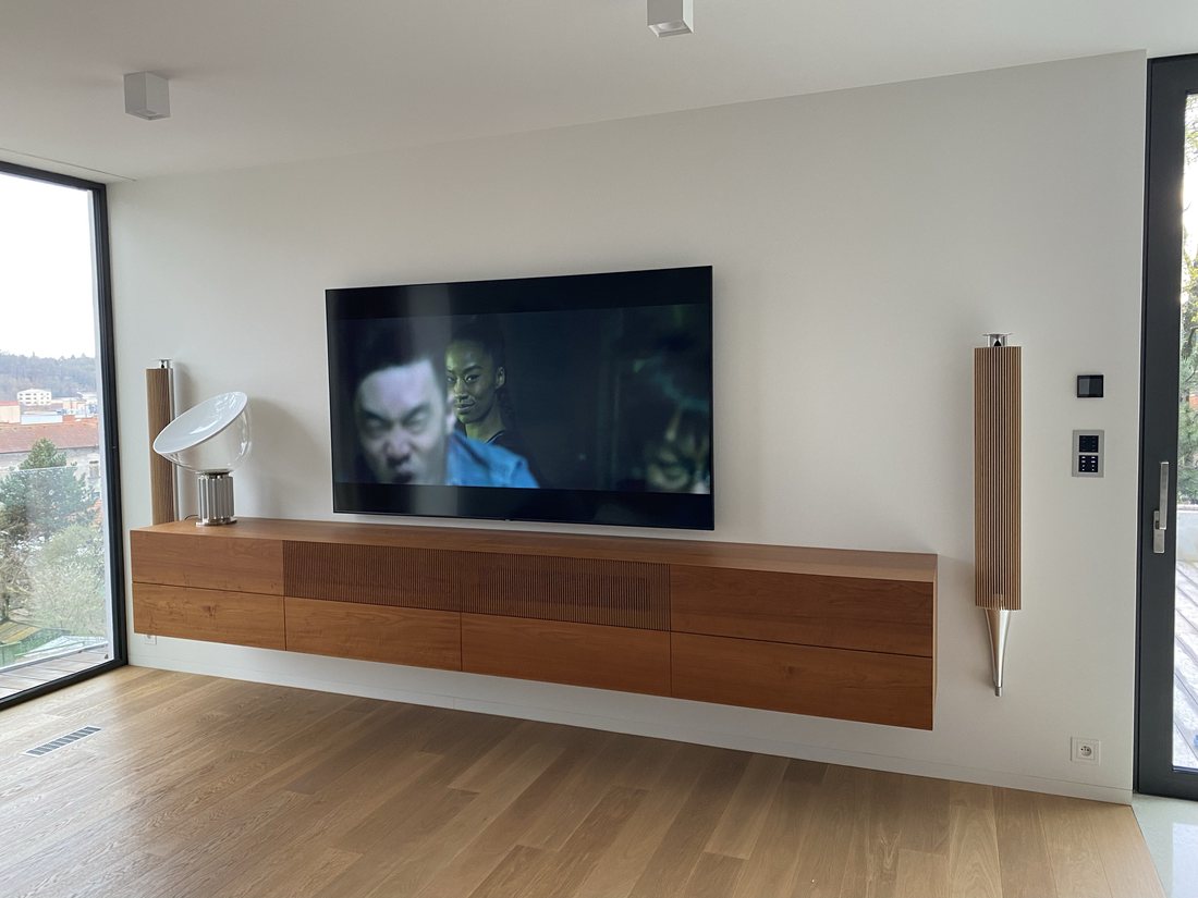 Velkoformátová OLED televize na zdi nad závěsnou dřevěnou komodou